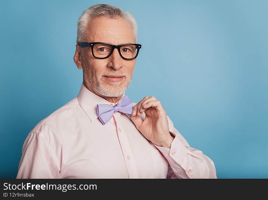 Photo of attractive aged man adjusting bow tie isolated on blue background.