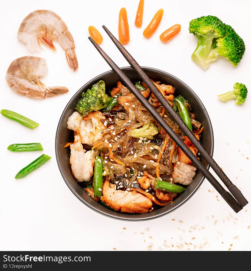 Stir fried noodles with shrimps and vegetables in a wok on white background, top view