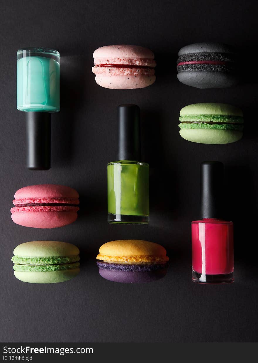 Different colored macarons and nail polishes on a black background
