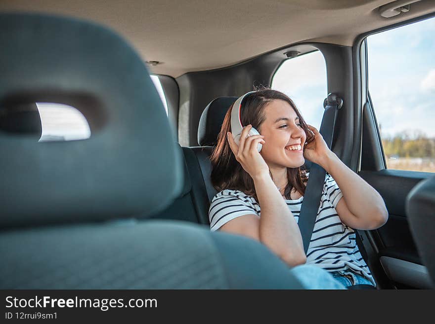 woman sitting at car rear sits listening music with headset copy space. sunny day
