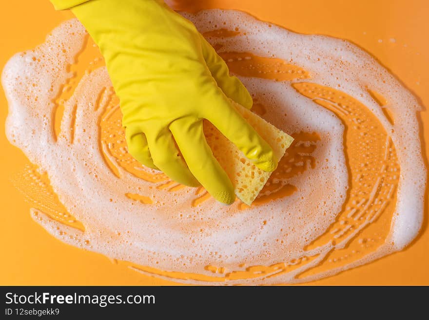 A hand in a rubber glove holds a cleaning sponge with foam on a bright yellow background. household chores and cleaning concept