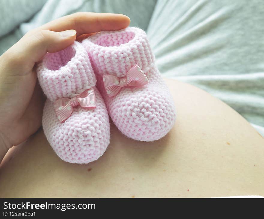 Closeup of pregnant woman holding pink baby booties on her belly.