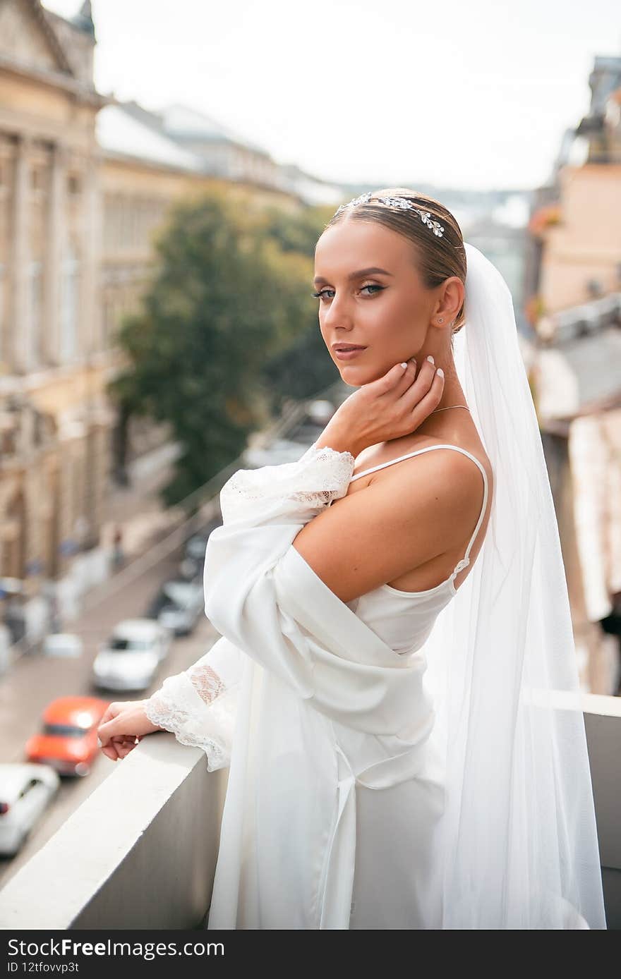 Attractive elegant woman with wedding makeup and hairstyle looking at camera while standing on balcony. Concept of tenderness and wedding day. Attractive elegant woman with wedding makeup and hairstyle looking at camera while standing on balcony. Concept of tenderness and wedding day