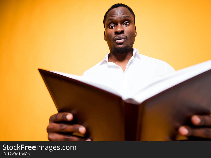 Handsome dark-skinned guy reading a book holding it in his hands and looking at it in surprise