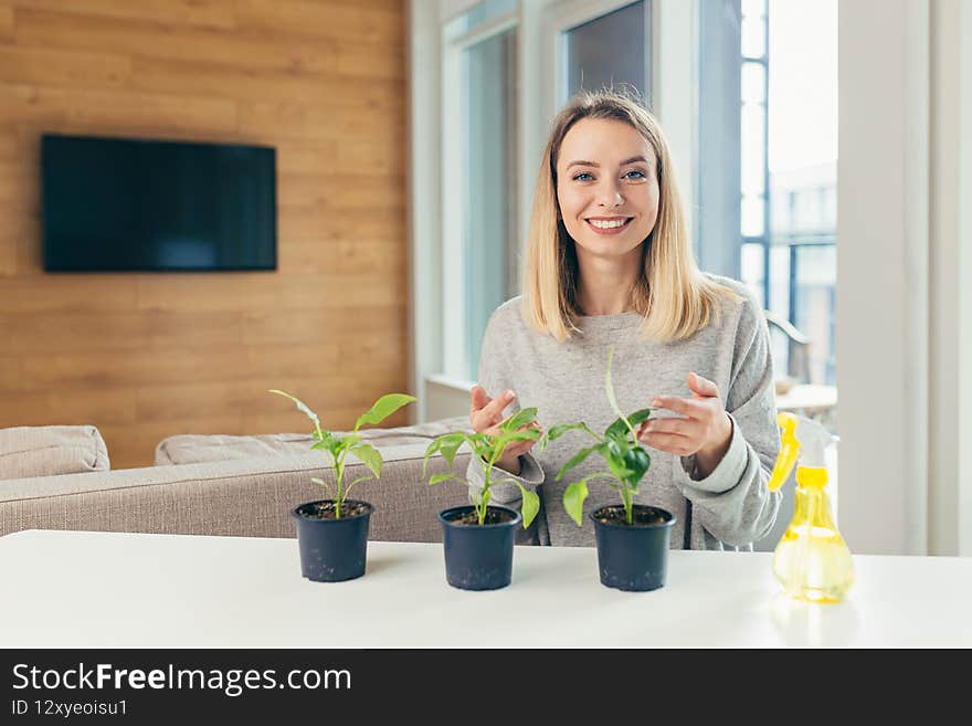 Young beautiful blonde woman, at home takes care of flower pots, pours flowers sitting at the table