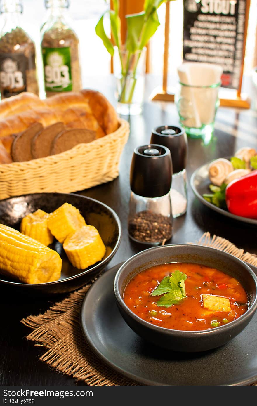 Mexican tomato, bean, bell pepper soup and corn in the dark bowl. Rustic style.