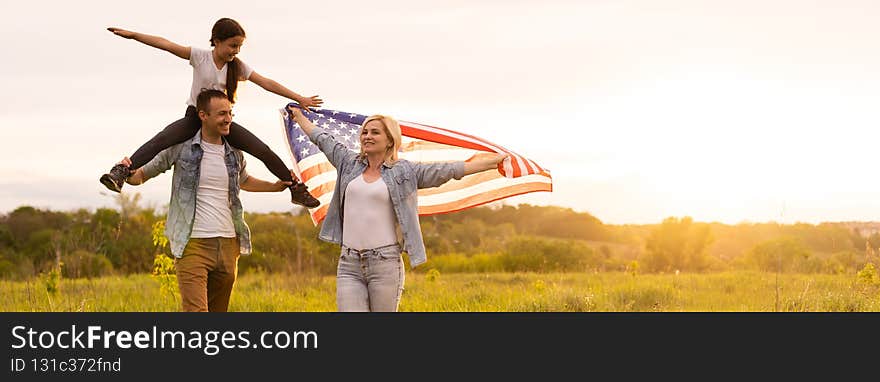 Beautiful family with the American flag in a field at sunset. Independence Day, 4th of July.