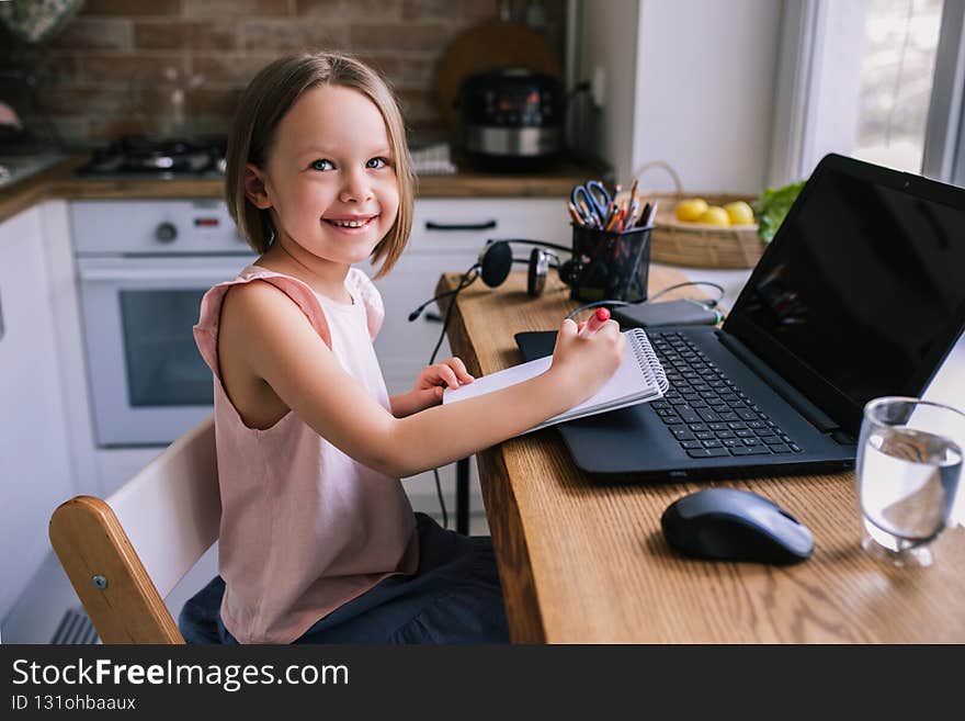 Pretty girl sitting at a table with a laptop during an online lesson. Distance education, homeschooling concept.