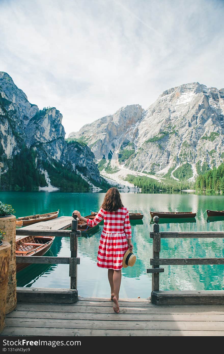 young gentle woman in red checkered dress barefoot walking by wooden stairs of boat station leads to lake. summer vacation