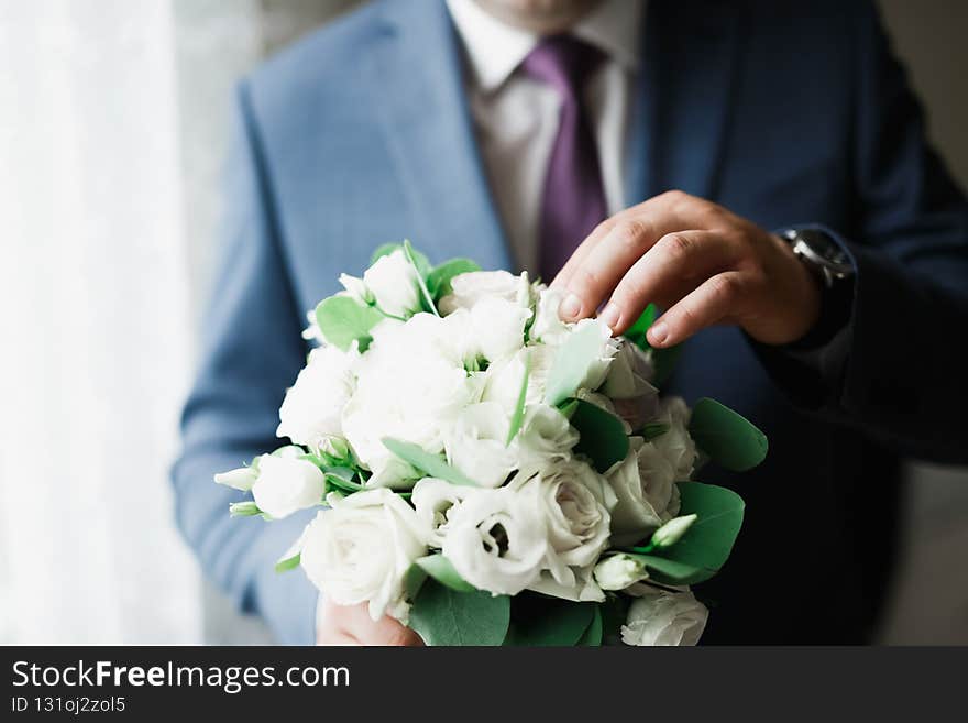 Beautiful man, groom holding big and beautiful wedding bouquet with flowers.