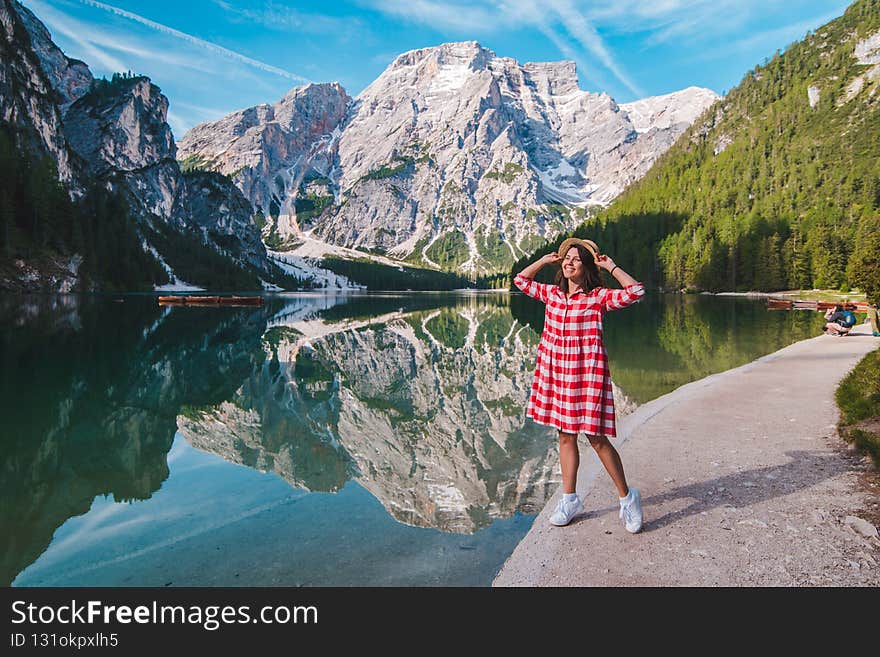 woman in red checkered dress with straw hat looking at mountain lake. summer vacation. travel concept