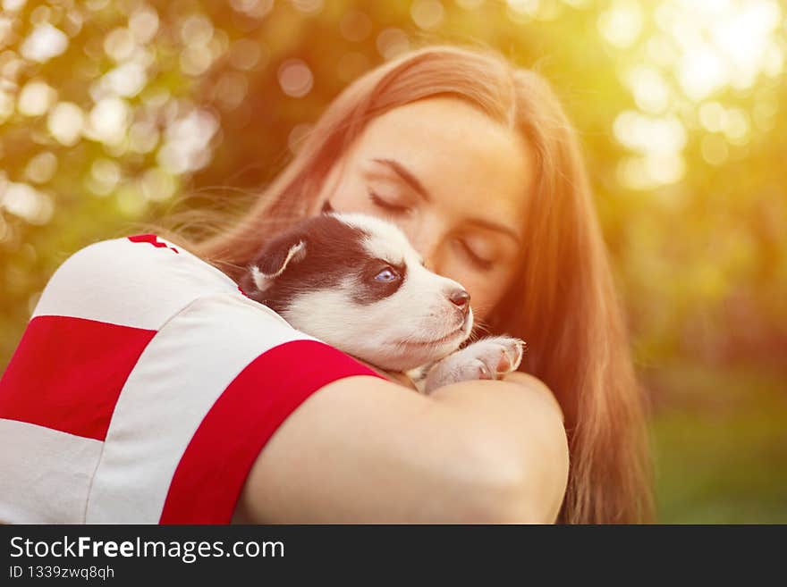 Beautiful woman in a striped t-shirt tenderly hugs a small husky puppy in the park outdoors.