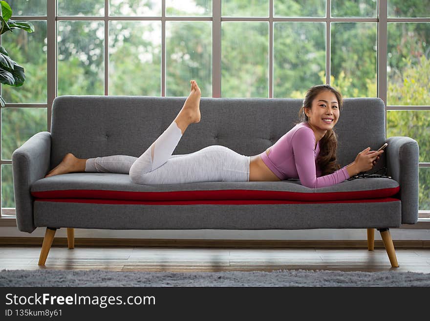 Asian woman play smartphone for chat with friend for stay at home in sport suit in living room