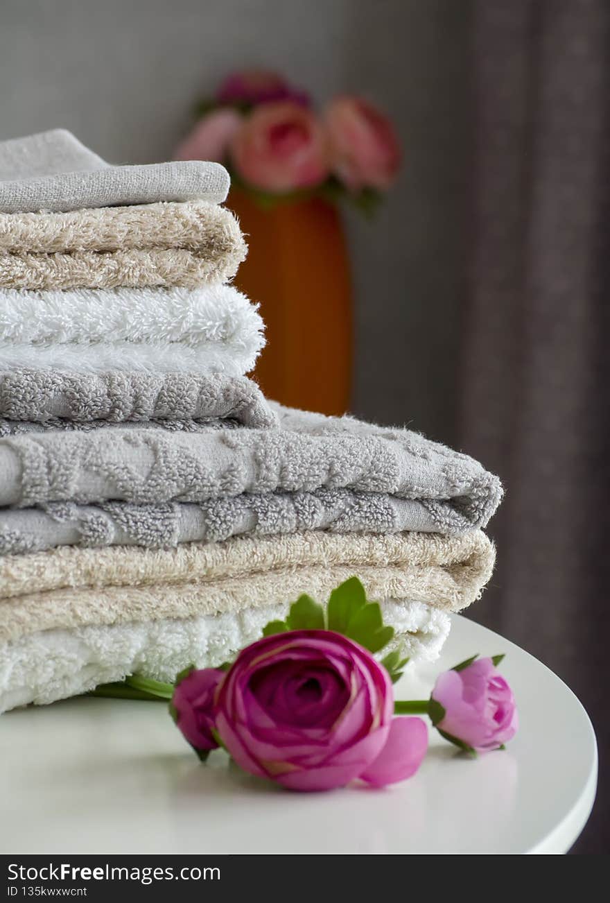 A stack of terry shower towels on a white table close-up next to artificial peony flowers.