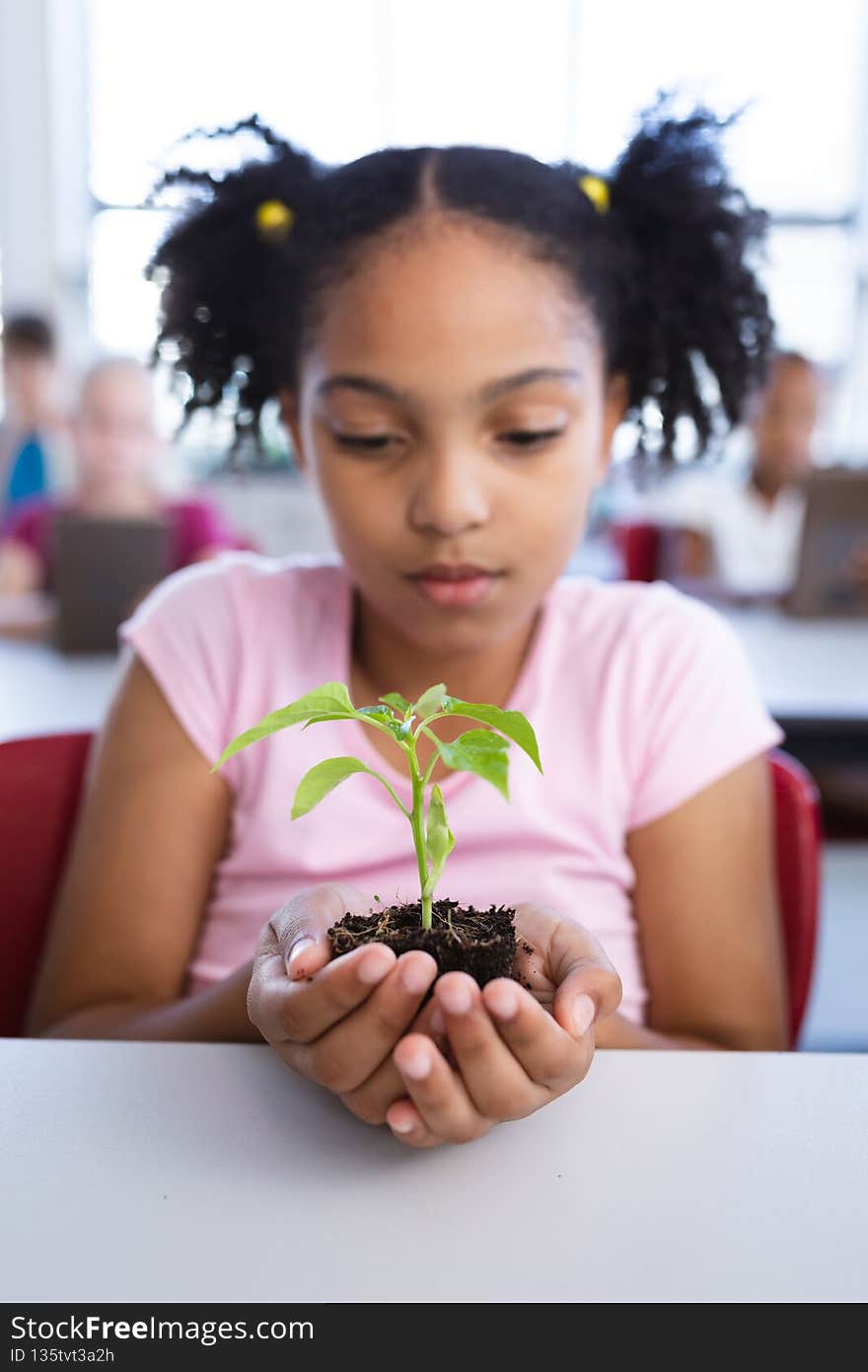 African american girl holding a plant seedling while sitting on her desk in class at school