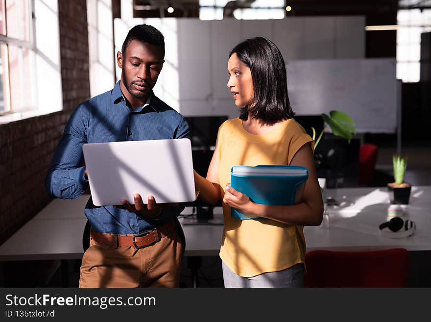 Serious diverse male and female colleague standing in office discussing, looking at laptop together
