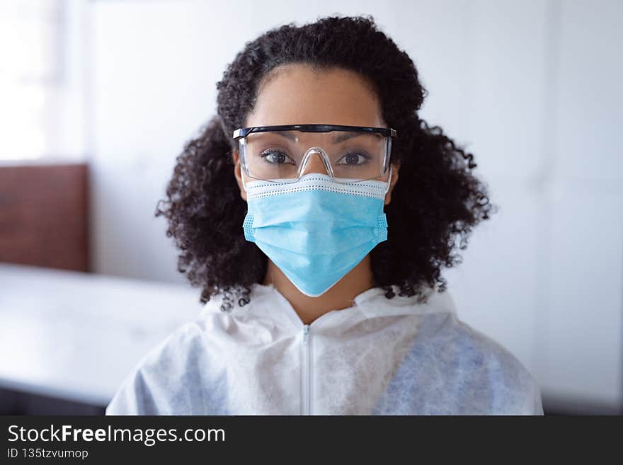 Portrait of african american female cleaner wearing ppe suit, glasses and mask in office. hygiene in business at a modern office during coronavirus covid 19 pandemic.