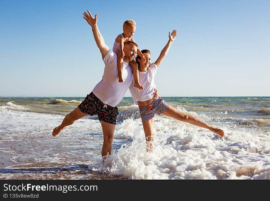 Happy family having fun on summer vacation. Happy son sits on his dad& x27;s neck. Cheerful young family on the seashore. Summer holidays for the whole family