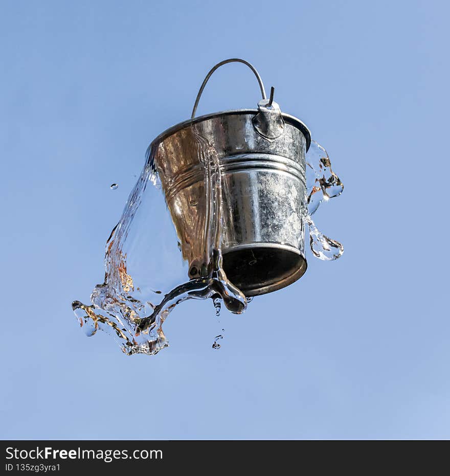 A falling bucket splashes water, on a background of blue sky