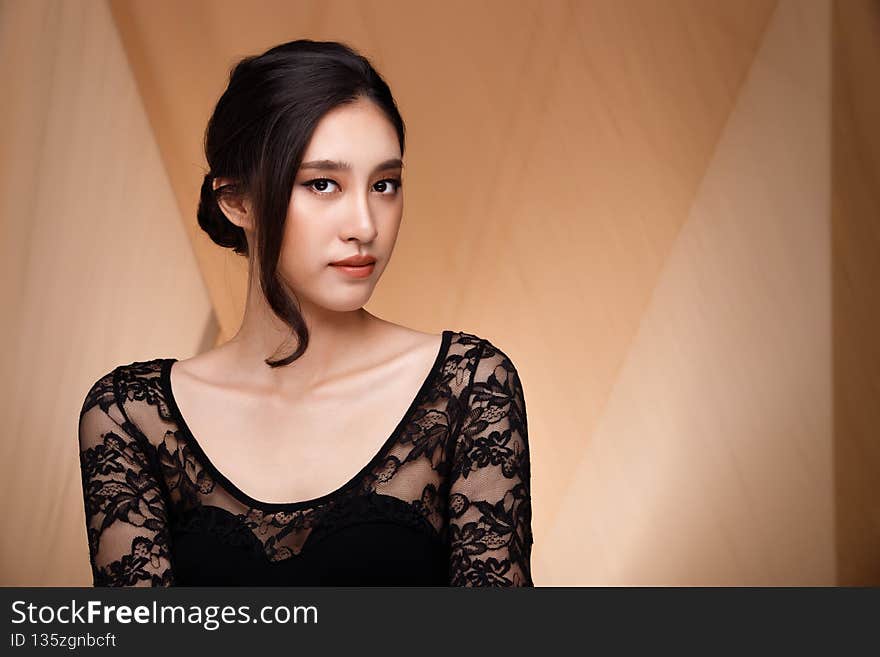 Fashion Beauty Woman has short straight black hair and express feeling. Portrait of Asian Thai girl wear lace dress with beige blazer suit over brown fabric drape cloth background