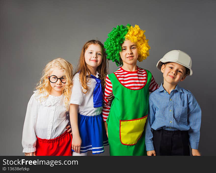 The group of children in a different professions costumes stay at the gray background. The kids are smiling and looking at the camera. The group of children in a different professions costumes stay at the gray background. The kids are smiling and looking at the camera