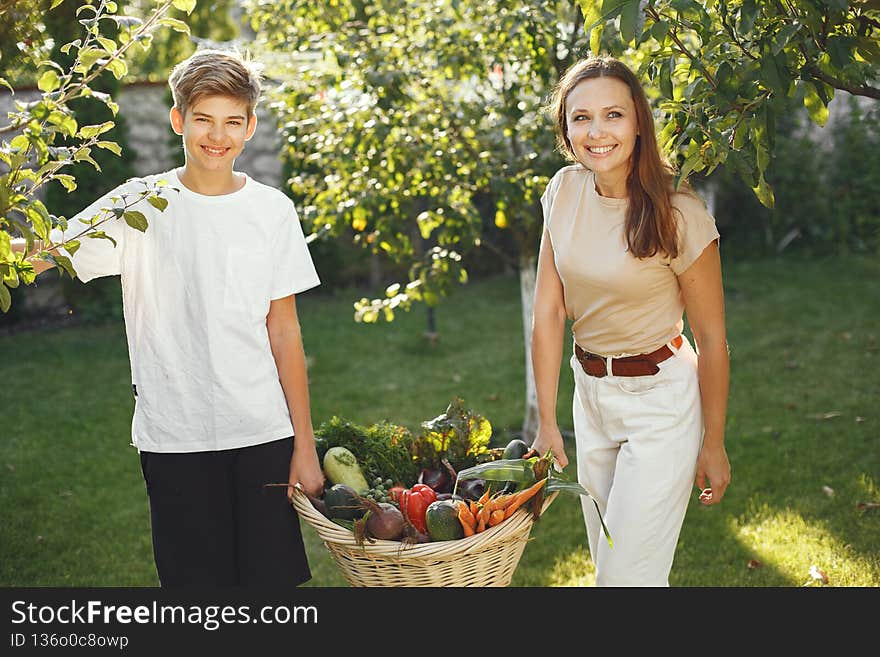 Cheerful family with organic vegetables in garden. Mixed organic vegetable in wicker basket. Mother with son in a backyard. Cheerful family with organic vegetables in garden. Mixed organic vegetable in wicker basket. Mother with son in a backyard.