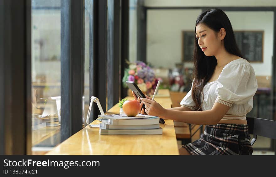 Side view of young female looking on digital tablet while doing homework in cafe