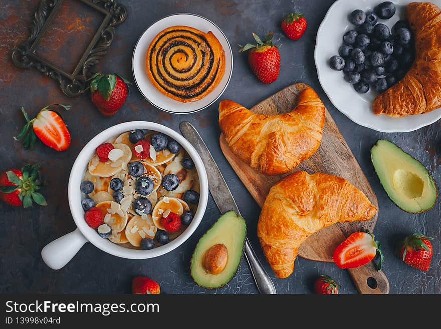 Breakfast, Mini pancakes with berries, croissants and avocado, Delicious summer food, Top view on a dark background