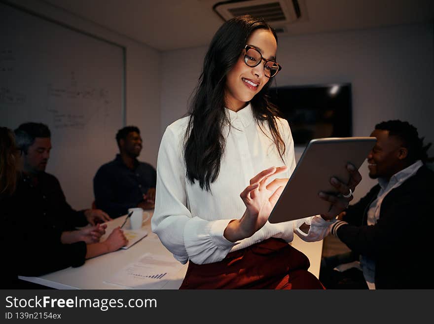 Portrait of a smiling young businesswoman sitting on desk in modern office using tablet device