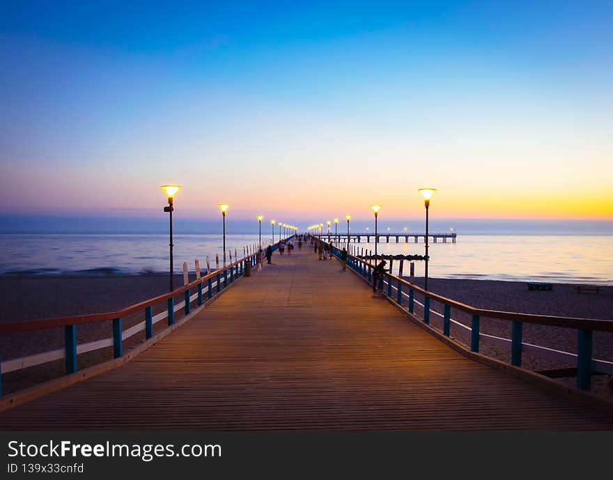 Illuminated romantic vintage Palanga pier after sunset with people walking in beautiful summer evening. Lithuania summer holiday landmarks destination