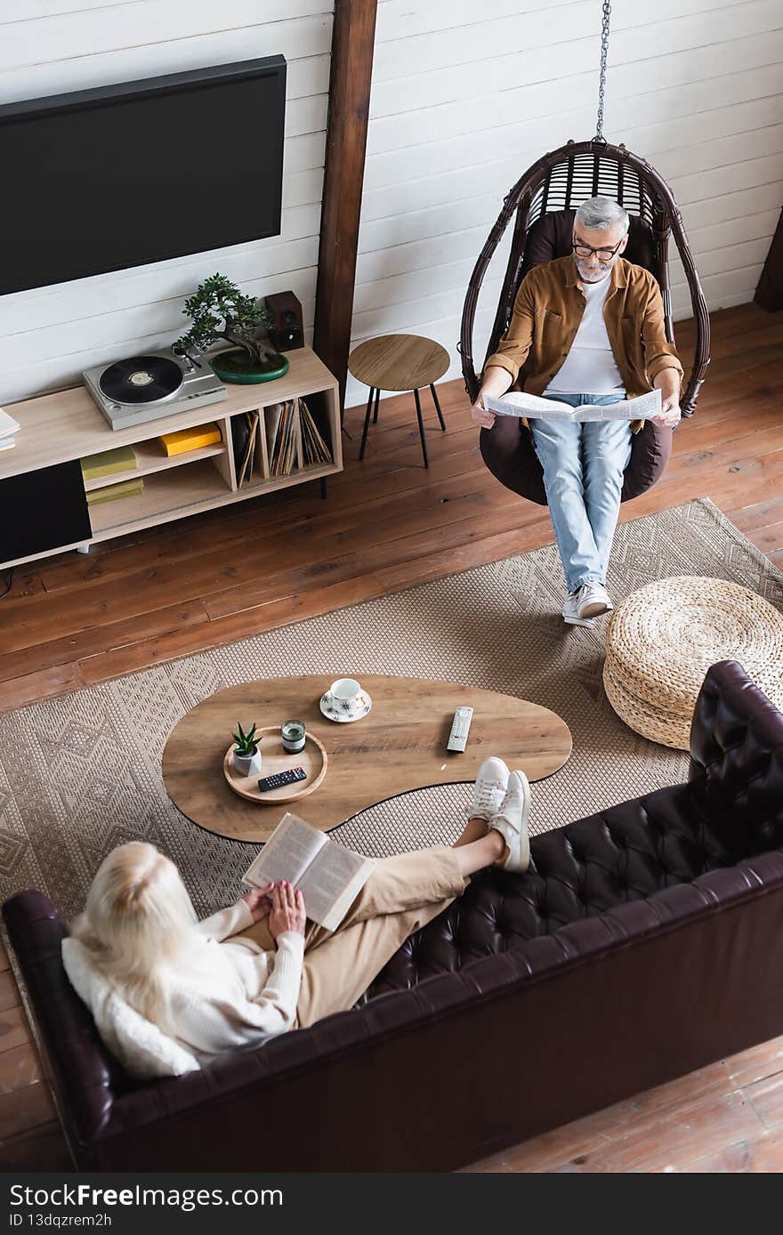 Overhead view of woman reading book on couch near husband with newspaper in hanging chair,stock image