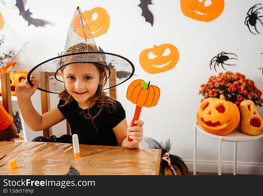 Adorable schoolgirls doing handmade paper decorations for autumn seasonal holidays. Engaged children working with paper and glue at wooden table. Halloween decor on white wall on a background. Adorable schoolgirls doing handmade paper decorations for autumn seasonal holidays. Engaged children working with paper and glue at wooden table. Halloween decor on white wall on a background.