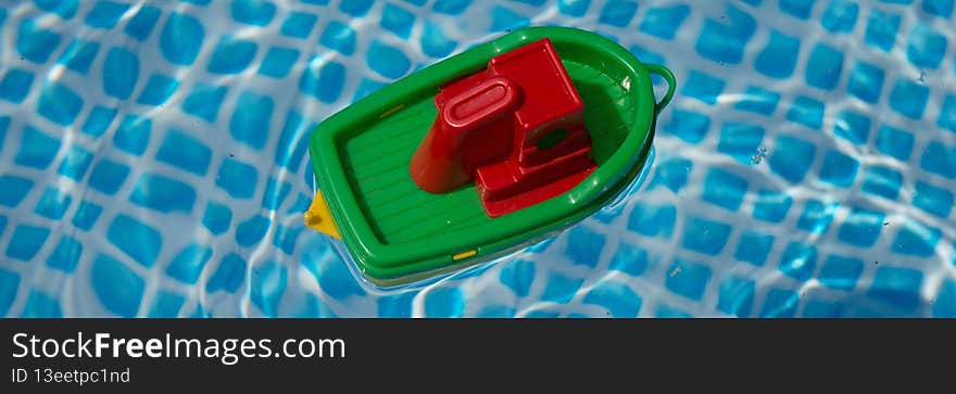 Small plastic toy boat floating in a swimming pool. Panorama