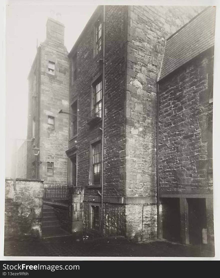 Photograph. There  are steps with a fence on the right, leading up from the court to a path along the building on the right and past the next building. A streetlamp stands at the side of the path. A washing pully prodrudes from the window of the second floor of the first building.

digital.nls.uk/74507004. Photograph. There  are steps with a fence on the right, leading up from the court to a path along the building on the right and past the next building. A streetlamp stands at the side of the path. A washing pully prodrudes from the window of the second floor of the first building.

digital.nls.uk/74507004