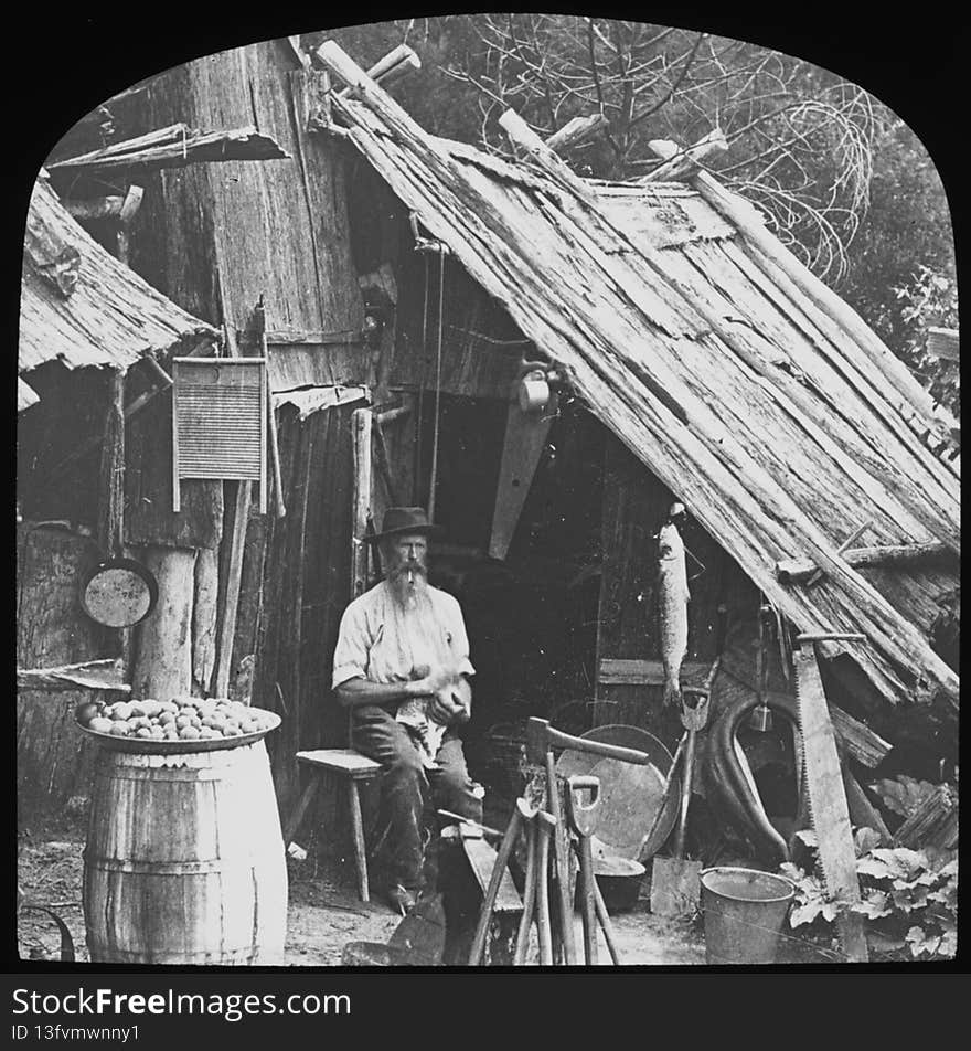 Man stroking a cat whilst sitting outside a bush humpy, Australia, ca. 1887 / Henry King