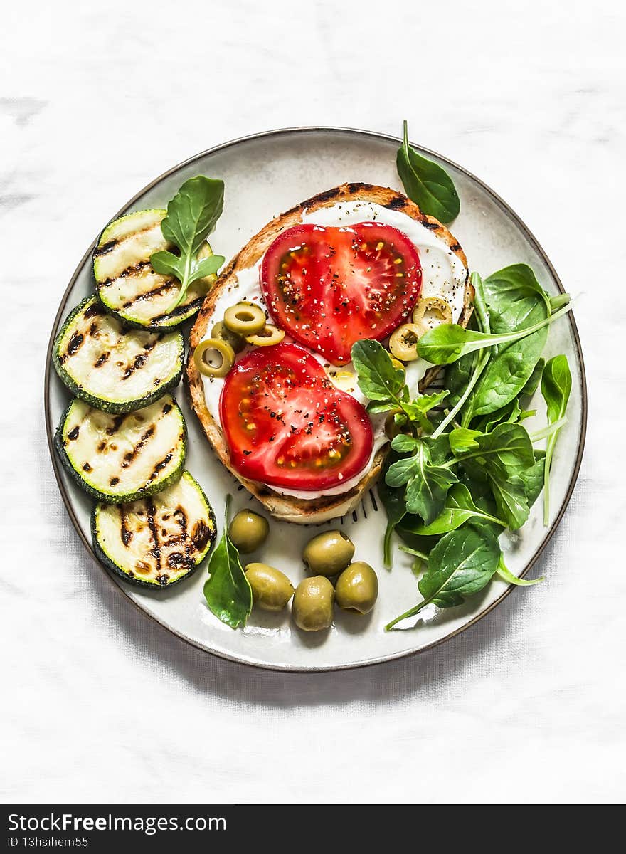 Sandwich with whipped ricotta, tomatoes, olives and grilled zucchini - delicious snack, tapas on a light background, top view