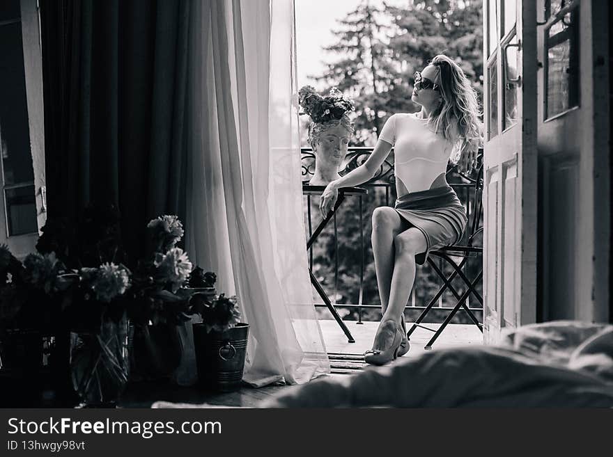A young girl in the morning in the doorway of the balcony sits at a table with flowers. High quality photo