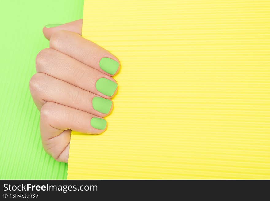 Female hand with green nail design. Green nail polish manicure. Woman hand hold yellow paper on green background