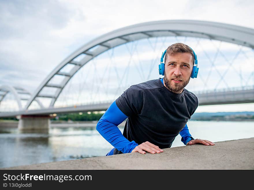 A portrait of an athlete wearing headphones and stretching by the river. Sport