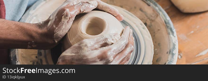 close up view of young african american men modeling wet clay on wheel with hands in pottery, banner,stock image