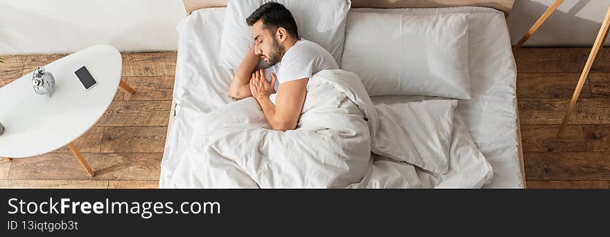 Side view of bearded man sleeping near smartphone on bedside table, banner,stock image