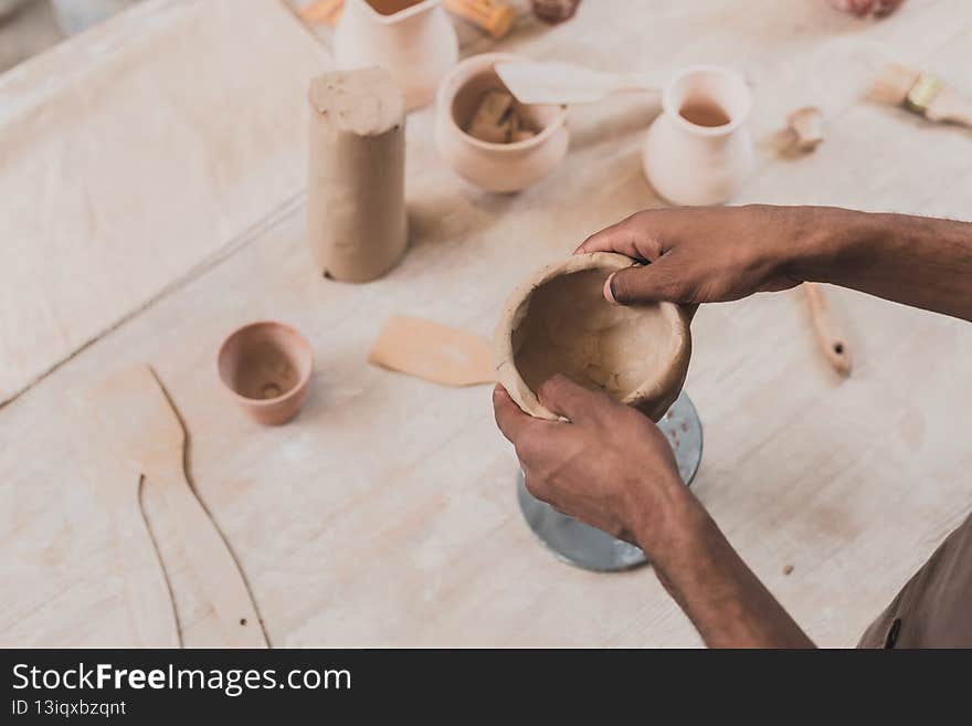 high angle view of young african american women sculpting clay pot with spatula in pottery,stock image