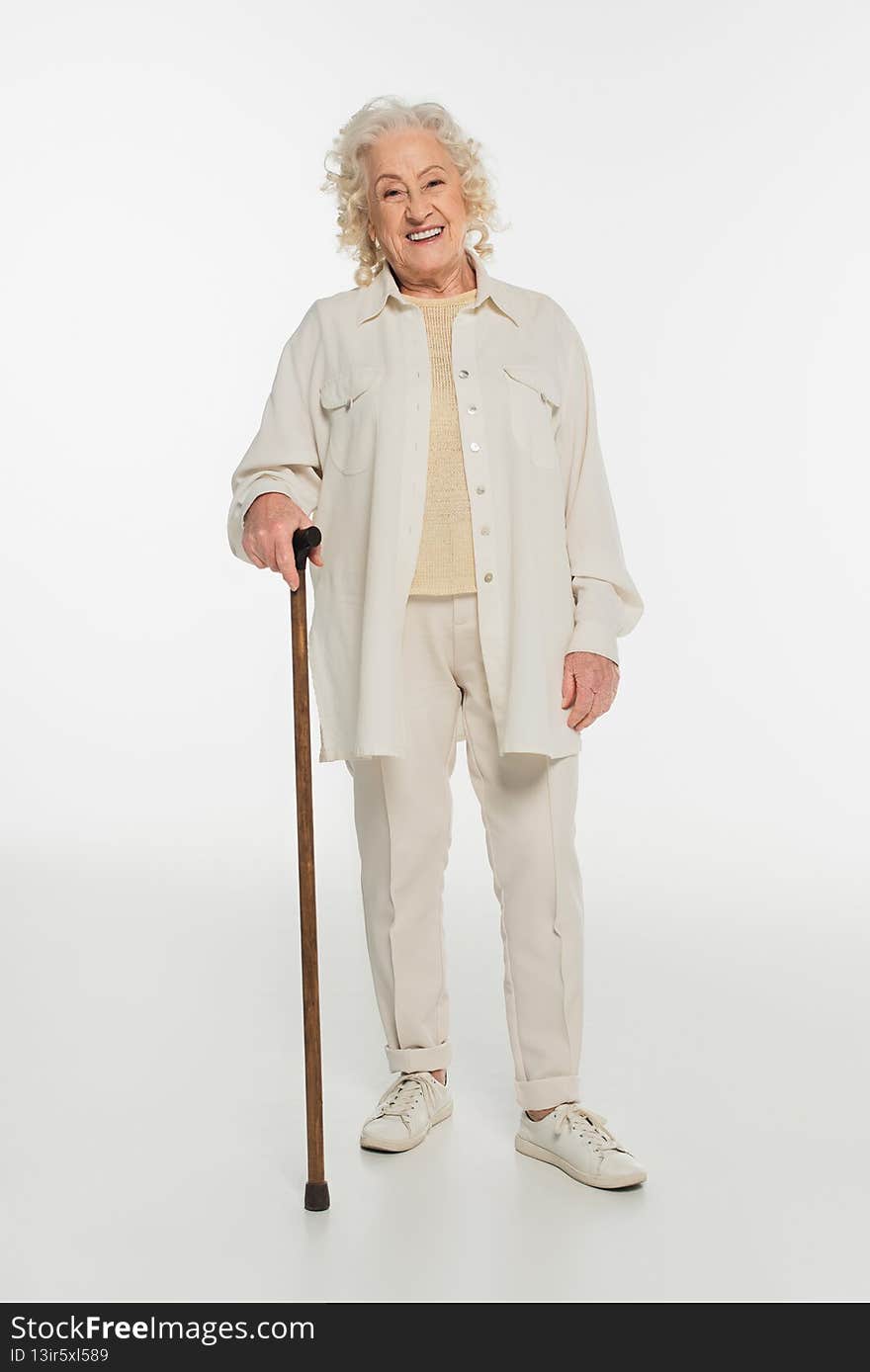 smiling elderly woman in casual clothes standing with walking stick on white,stock image