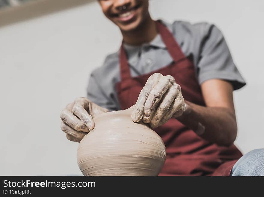 partial view of young african american men in apron sculpting clay pot in pottery,stock image