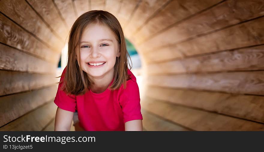 Smiling little girl sitting in wooden pipe, panoramic orientation. Smiling little girl sitting in wooden pipe, panoramic orientation