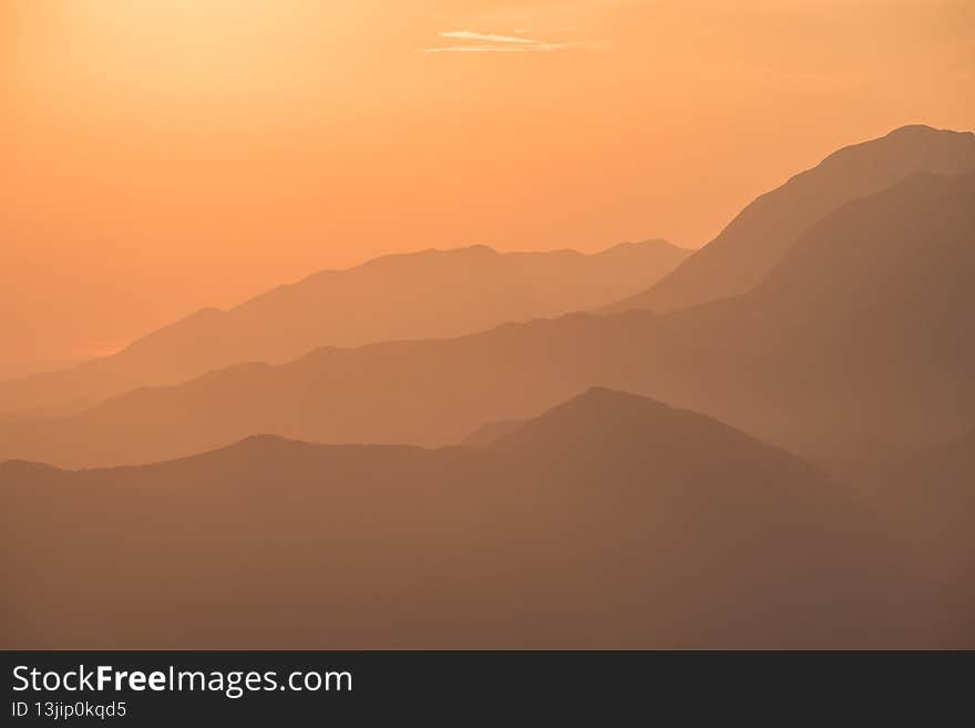 Orange sunset over Montenegrin mountains with small cloud in the sky