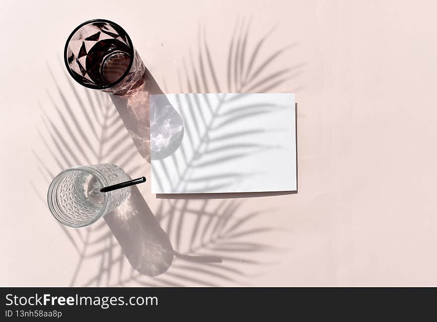 Summer tropical mockup still life flat lay. Empty blank invitation card, cocktail glass on beige background. Palm leaves shadow. Reflection. Eco minimal concept for wedding, vacation or relax