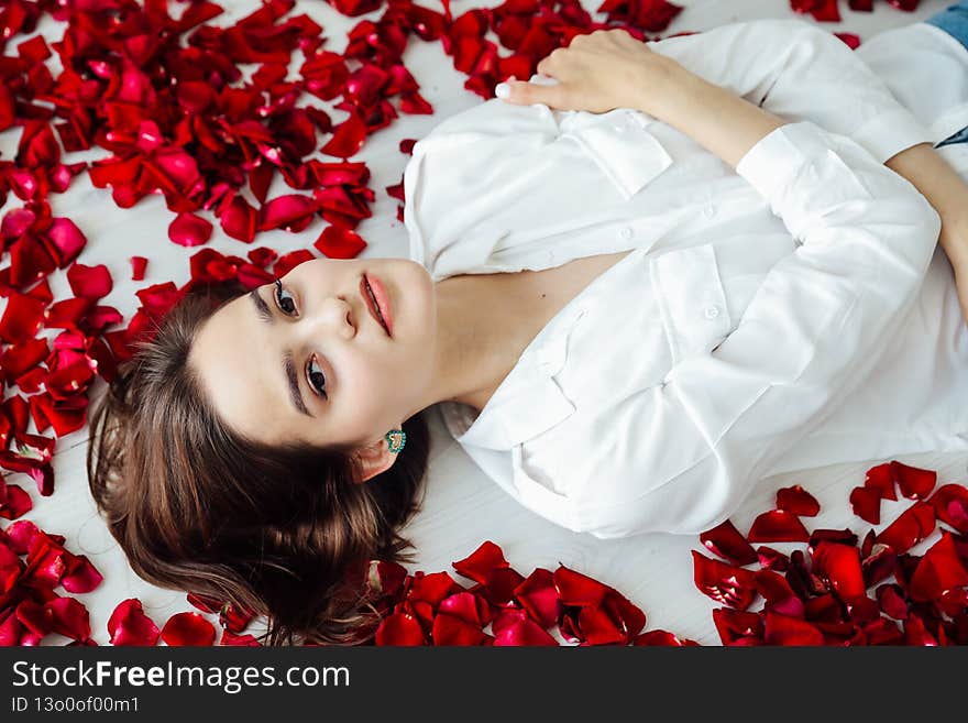 beautiful woman lies among the red petals of rose flowers