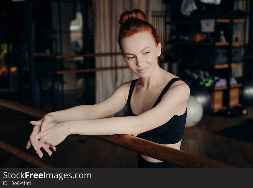 Pretty young red haired woman leaning on ballet barre