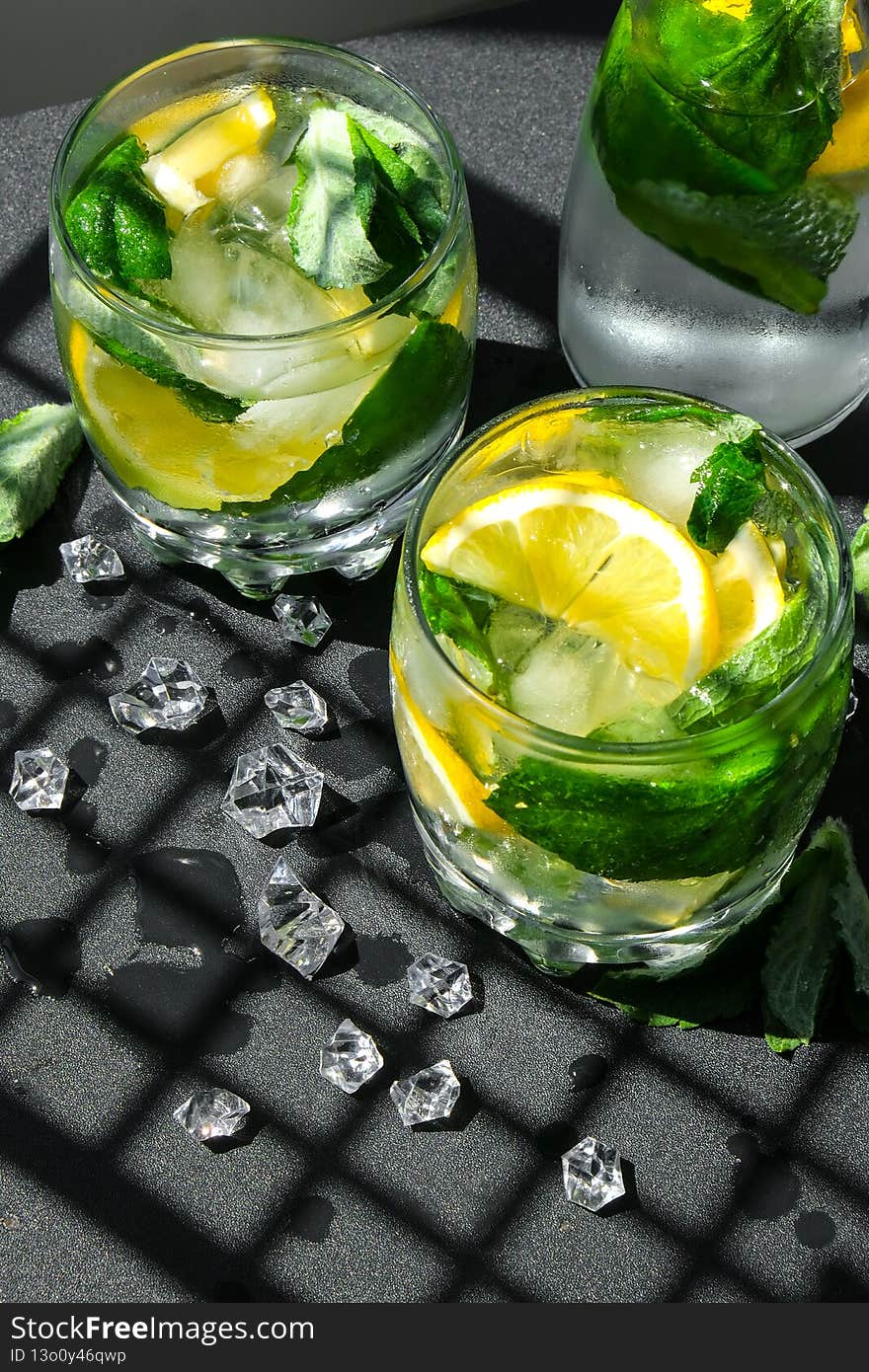 Mojito refreshing cocktail, alcohol drink. Lemonade with lemon and mint leaves on dark background. Trendy shadows Ice